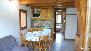 A cozy room with a round table and chairs, a sofa, wooden cabinets, and a kitchen area with a tiled backsplash.