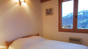 A bedroom with a bed, a wooden headboard, a nightstand, a window with a view of mountains, and a wall-mounted heater.