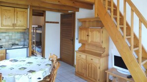 A wooden staircase leading to an upper level, a dining area with a table and chairs, and a kitchen with wooden cabinets and a tiled backsplash.
