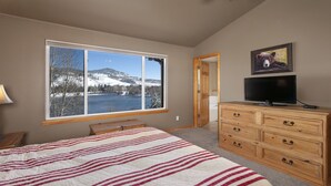A bedroom with a large window, a bed with a striped blanket, a dresser, and a television. - Private Lakefront Luxury in the heart of Ski Country, Mountain Views (Silverthorne)