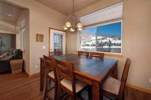 A dining area with a wooden table and chairs, a chandelier, a window with a snowy mountain view, and a door leading to another room. - Private Lakefront Luxury in the heart of Ski Country, Mountain Views (Silverthorne)