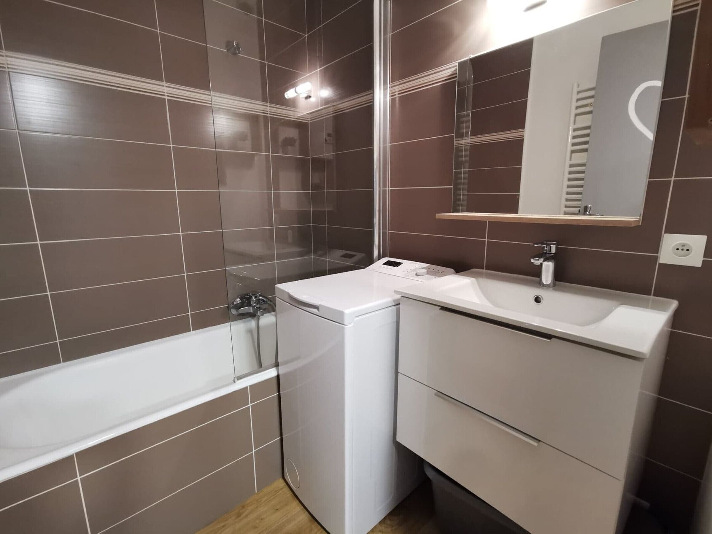 A bathroom with a bathtub, a washing machine, and a sink with a mirror above it.
