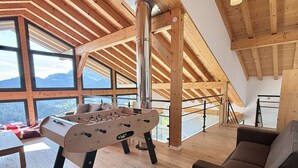 Une pièce spacieuse avec un plafond en bois, un baby-foot, un canapé et de grandes fenêtres offrant une vue sur les montagnes.
