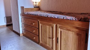 A bedroom with a wooden bed, a nightstand, a dresser, and a wall-mounted light. - Studio/Cabin with Mezzanine - Near Slopes, 5 People (Notre-Dame-de-Bellecombe)