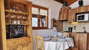 A cozy kitchen with wooden cabinets, a dining table set for four, and a television on a wooden cabinet. - Studio/Cabin with Mezzanine - Near Slopes, 5 People (Notre-Dame-de-Bellecombe)
