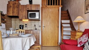 A compact living space with a kitchenette, a dining area, and a red sofa. - Studio/Cabin with Mezzanine - Near Slopes, 5 People (Notre-Dame-de-Bellecombe)