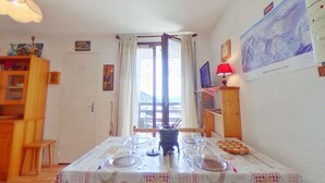 Un coin repas avec une table dressée pour quatre personnes, un meuble en bois, un ordinateur posé sur un bureau et une fenêtre avec des rideaux.