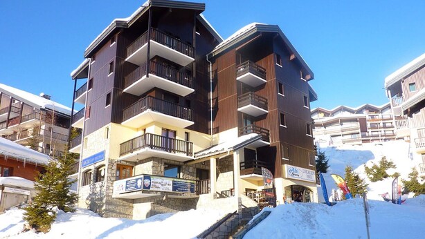 Un hôtel à plusieurs étages, doté de balcons et d’une façade en pierre, avec une piste de ski en arrière-plan.
