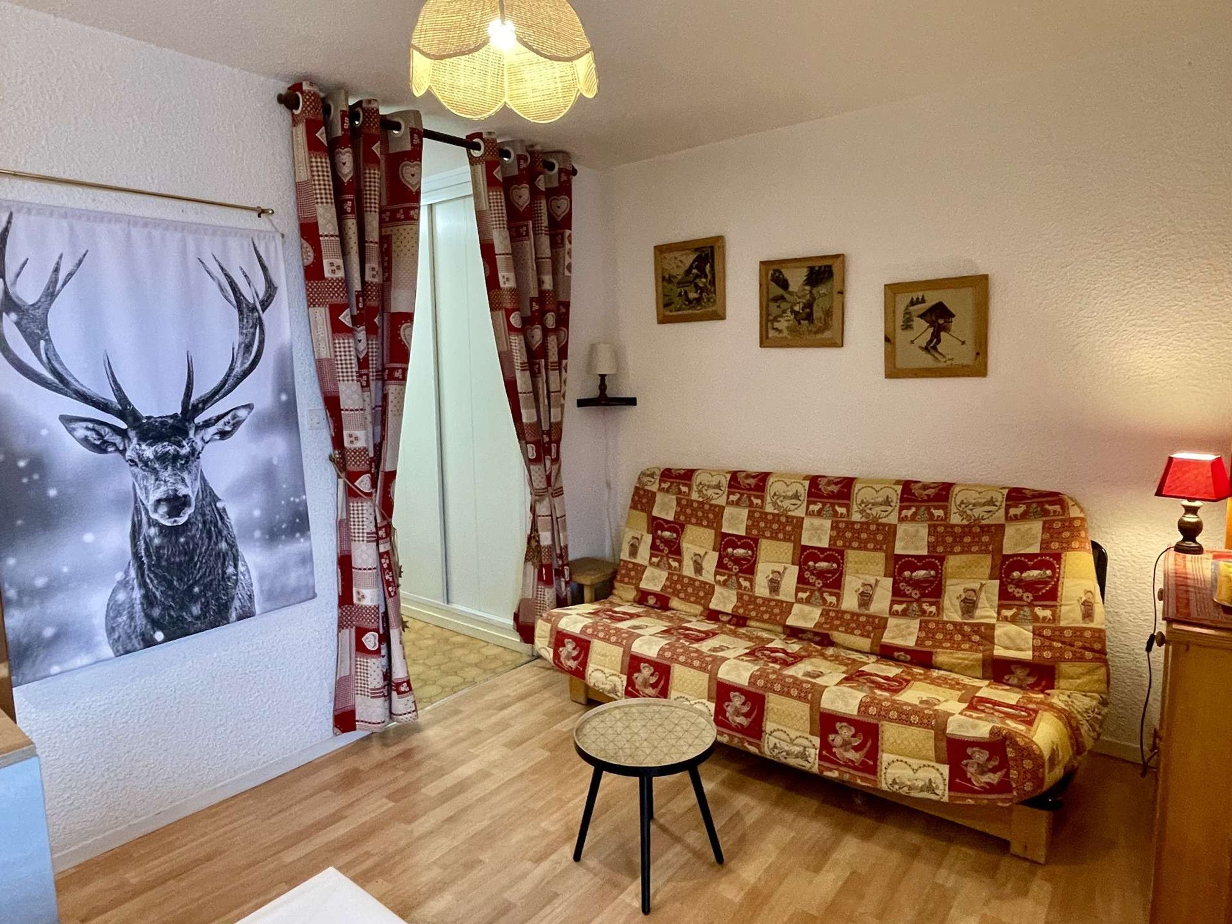 Una habitación acogedora con un sofá estampado, un taburete pequeño, una obra de arte con ciervo enmarcado y una lámpara en una mesita de noche.