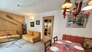 A cozy living room with a sofa, a dining table set for four, and a wooden wall.