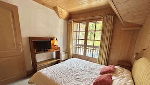 A bedroom with a bed, a television on a wooden shelf, and a window with curtains.