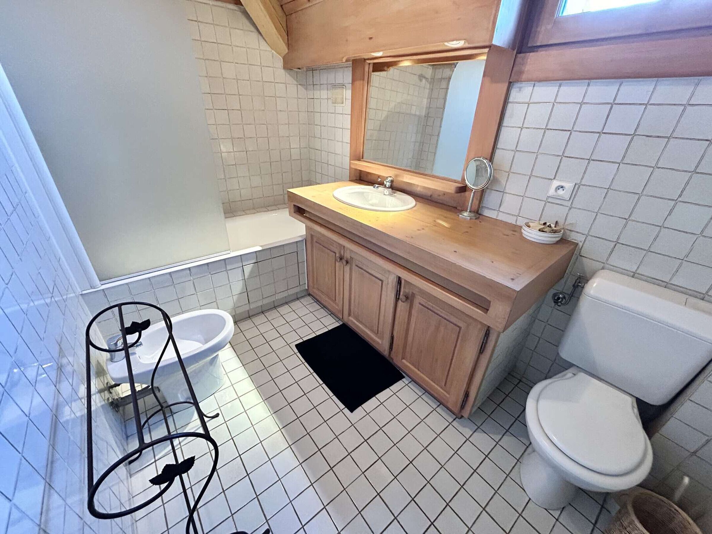 Une salle de bain avec un meuble-lavabo en bois, un lavabo blanc, un miroir, des toilettes et un bidet.