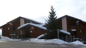 A two-story wooden building with a covered entrance and a sign indicating danger. Snow is piled up in front of the building. - Studio cabin Les Saisies 4 pers, near slopes (Les Saisies)