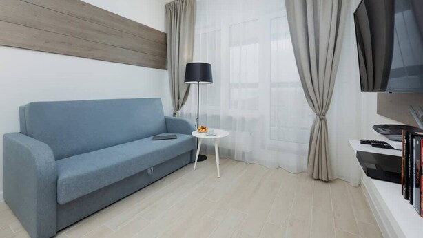 A modern living room with a blue sofa, a small white table, a floor lamp, a TV, and a bookshelf.