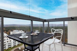 Ein Balkon mit Tisch und Stühlen, Blick auf Gebäude und Hügel, und ein klarer Himmel.