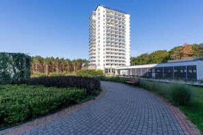 A modern hotel with a tall, multi-story structure, a paved walkway, and a landscaped area with greenery.