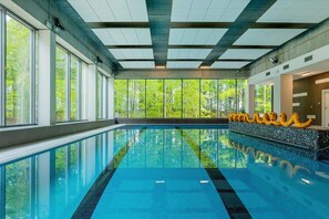 An indoor swimming pool with clear glass walls, a tiled floor, and a view of greenery outside.