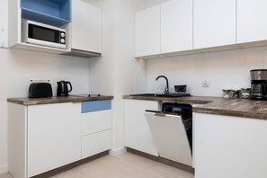 Une cuisine compacte avec des meubles blancs, un four à micro-ondes, une machine à café et un lave-vaisselle.