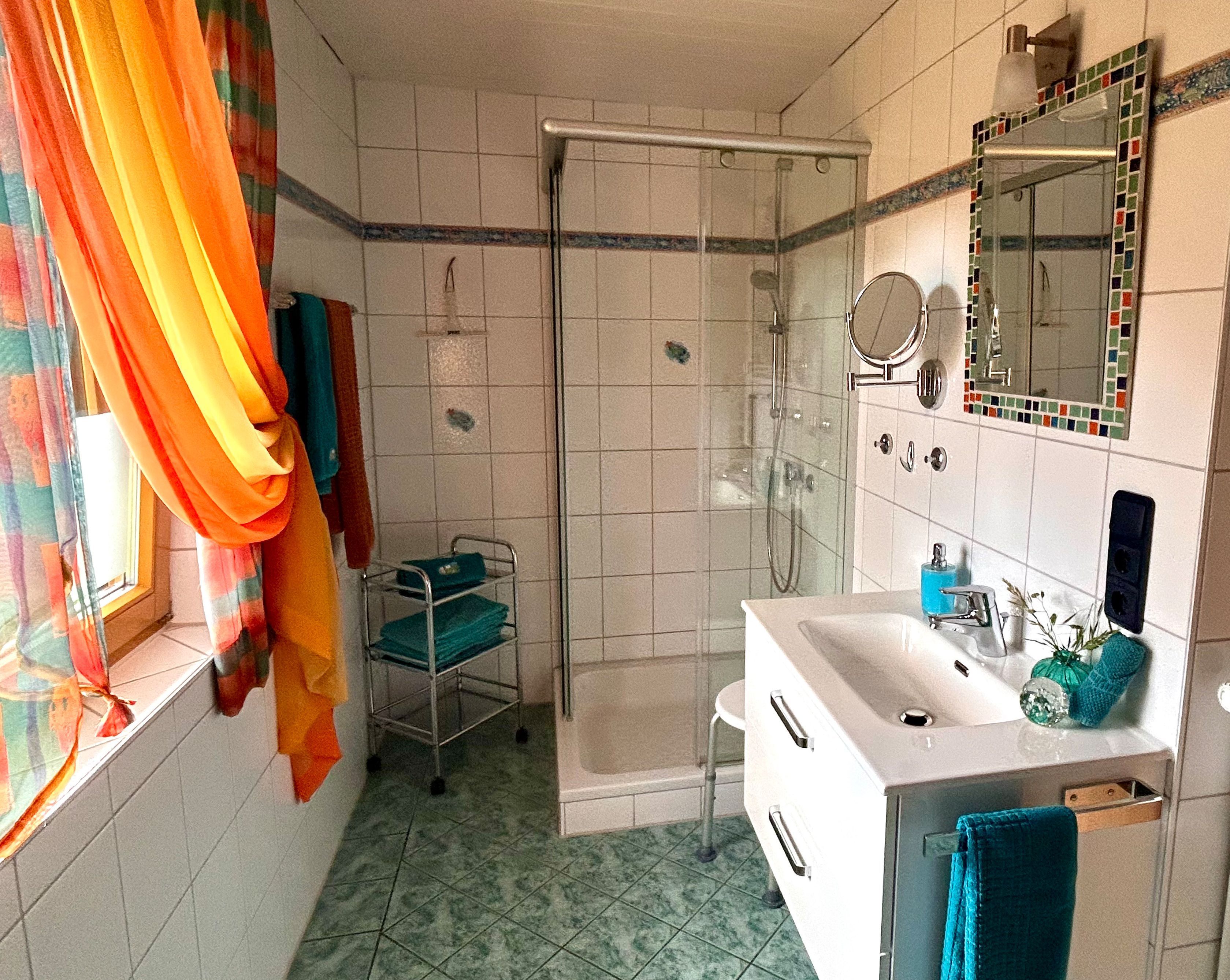 Ein Badezimmer mit Dusche, Waschbecken, Spiegel und einem Fenster mit Vorhängen.