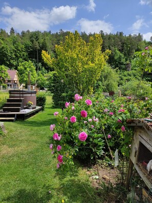 Ein Garten mit rosa Blumen, einer Holzkonstruktion und bewaldeter Landschaft im Hintergrund.
