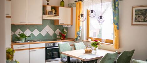 A compact kitchen with white cabinets, a dining area with a table and chairs, and a window with curtains.