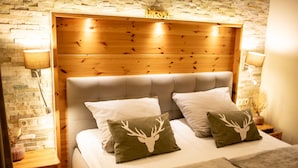 Un lit avec une tête de lit en bois, deux oreillers ornés de motifs représentant des têtes de cerf et un mur en briques.