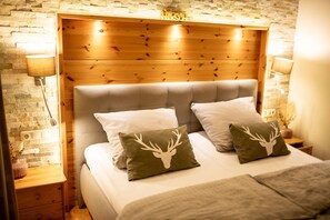 A bed with a wooden headboard, two pillows with deer head designs, and a brick wall.