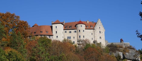 A castle-like building with multiple towers and a red roof, surrounded by autumn foliage.
