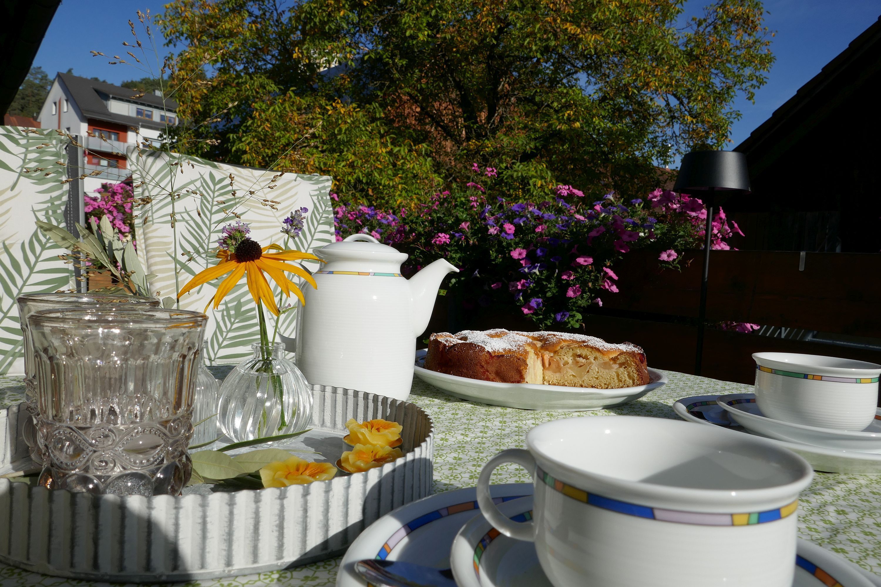 A table set with a teapot, cups, saucers, a plate with a cake, and a vase with flowers.