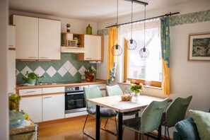 A compact kitchen with white cabinets, a dining area with a table and chairs, and a window with curtains.