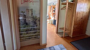 Une pièce avec une armoire en bois, une porte ornée d’une fresque représentant un château, un meuble en bois contenant des vêtements pliés et un sol recouvert d’une moquette.