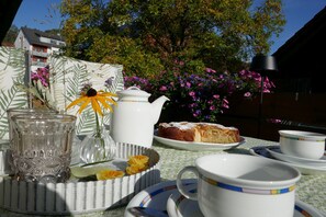 A table set with a teapot, cups, saucers, a plate with a cake, and a vase with flowers.