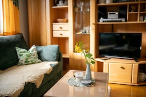 A living room with a sofa, a coffee table with a vase and a glass, a television, and wooden shelves with various items.