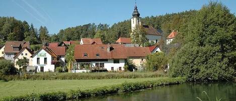A riverside village with houses, a church, and a tower.