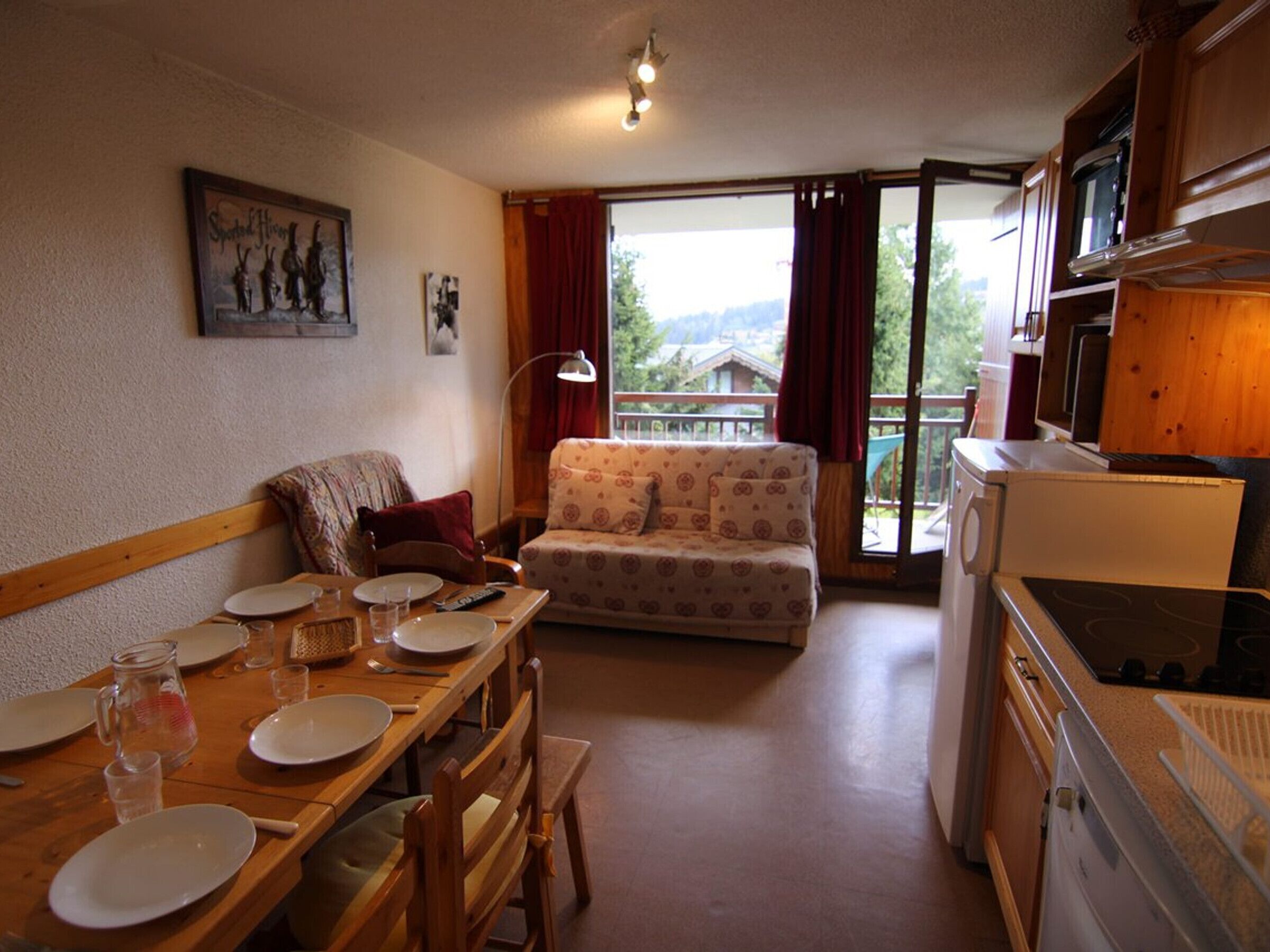 A cozy living room with a sofa, dining table set for four, and a kitchen area with a stove.