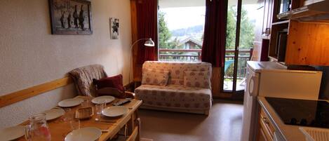 A cozy living room with a sofa, dining table set for four, and a kitchen area with a stove.