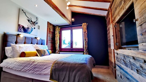 A bedroom with a bed, a window with curtains, a television, and wooden beams on the ceiling. - Cozy chalet with fireplace and parking, for 8 people (Les Gets)