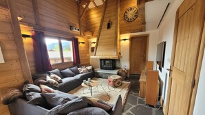 A cozy log cabin interior with a stone fireplace, a sofa, a coffee table, and a wooden ceiling. - Cozy chalet with fireplace and parking, for 8 people (Les Gets)