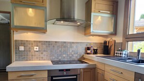 A modern kitchen with a Bosch dishwasher, wooden cabinets, a tiled backsplash, and a window providing natural light. - Cozy chalet with fireplace and parking, for 8 people (Les Gets)