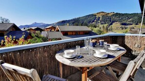 A wooden table with chairs on a balcony overlooking a mountainous landscape. - Cozy chalet with fireplace and parking, for 8 people (Les Gets)