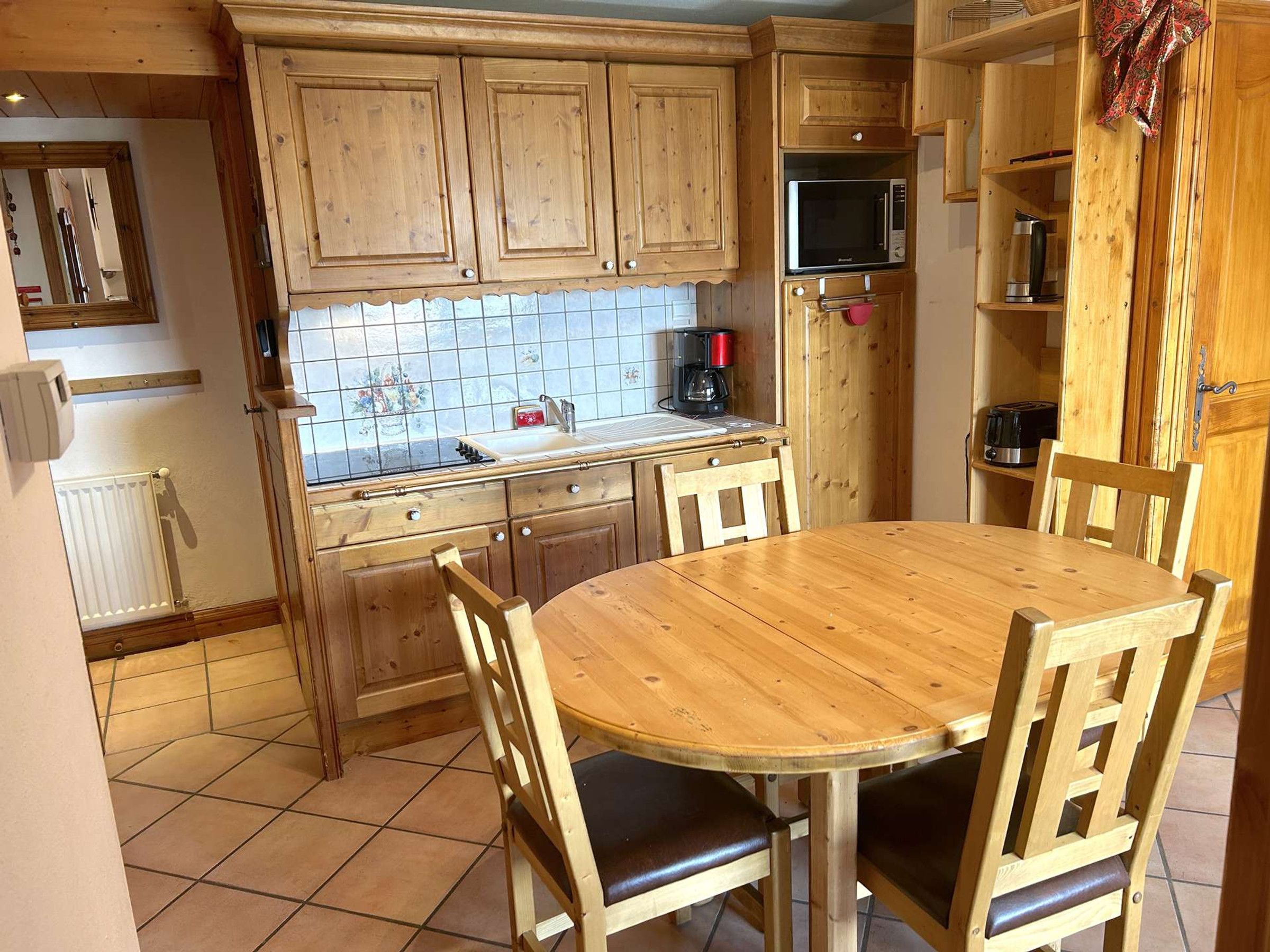Une cuisine avec des meubles de rangement en bois, un four à micro-ondes, une machine à café et une table ronde en bois, accompagnée de chaises.