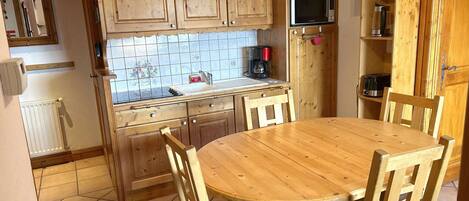 Une cuisine avec des meubles de rangement en bois, un four à micro-ondes, une machine à café et une table ronde en bois, accompagnée de chaises.