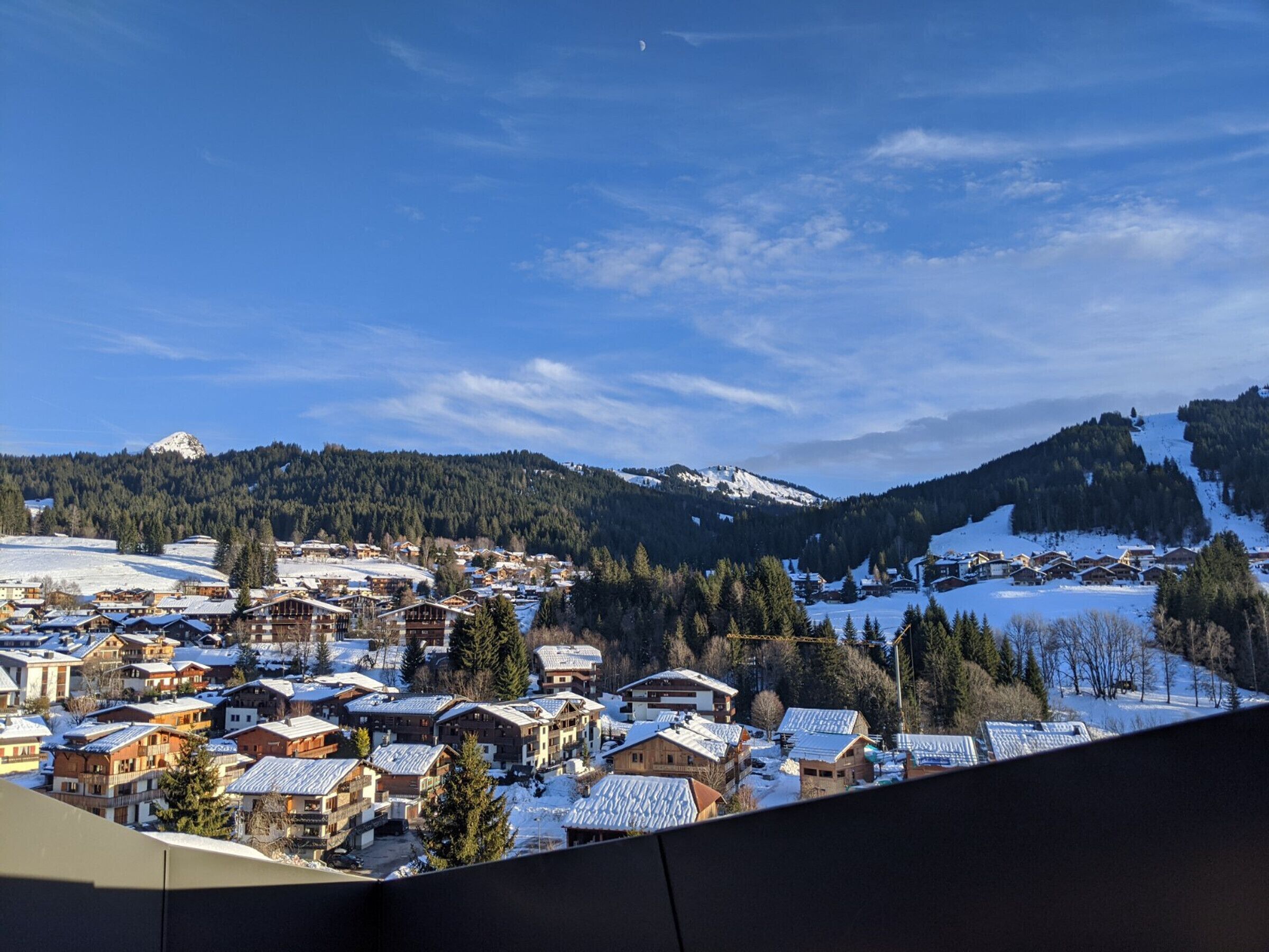 A snow-covered village with traditional wooden houses, a clear sky, and mountains in the background.