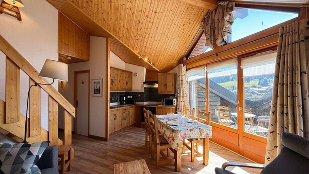 A cozy cabin interior with a dining area, kitchen, and large windows offering a view. - Cozy apartment in Les Gets with balcony and parking (Les Gets)