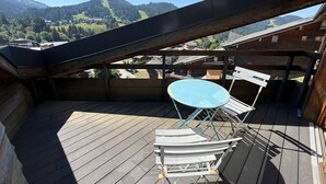 A wooden deck with a table and chairs, overlooking a mountainous landscape. - Cozy apartment in Les Gets with balcony and parking (Les Gets)