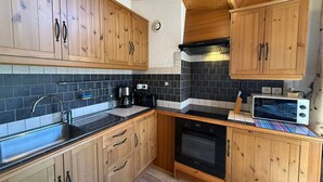 A kitchen with wooden cabinets, a black stove, and a microwave. - Cozy apartment in Les Gets with balcony and parking (Les Gets)