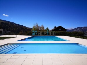 Ein rechteckiger Pool mit Fliesen umgeben, umzäunt und vor einer Bergkulisse unter blauem Himmel gelegen.