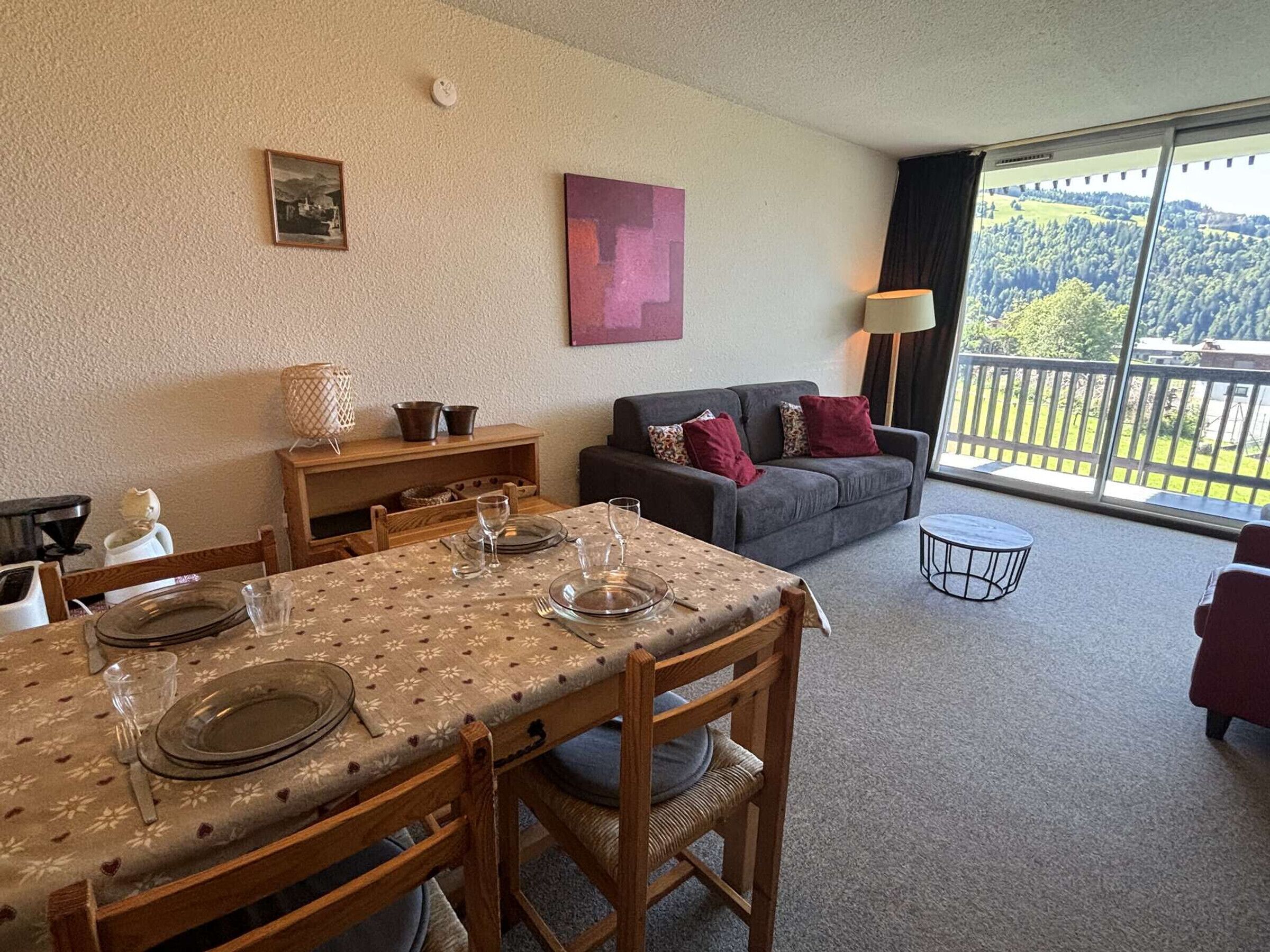 Un área de comedor con una mesa preparada para cuatro personas, un sofá y un balcón con vistas.