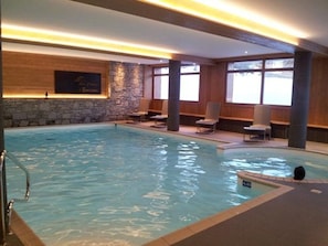 Une piscine intérieure avec un mur en pierre, un lambris en bois et des espaces aménagés pour s’asseoir.