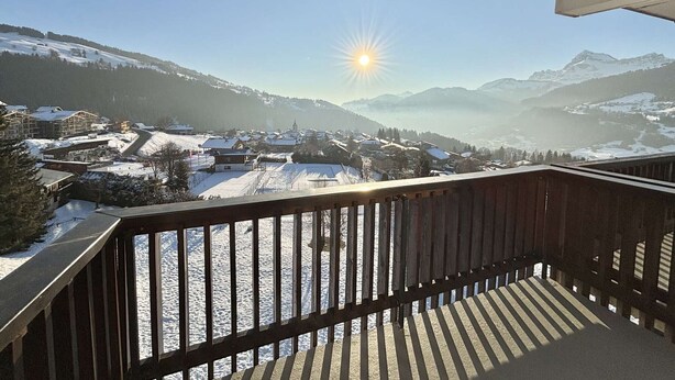 A balcony with a view of a snow-covered village and mountains under a clear sky.